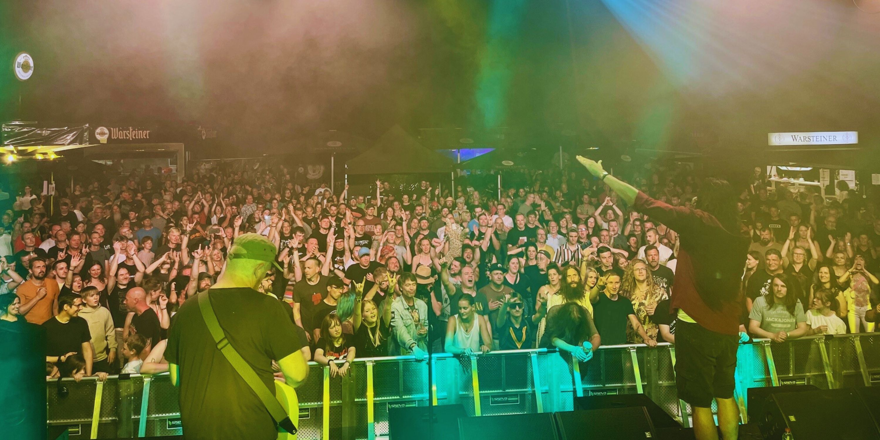 Titelbild Uferrock Eine Band spielt vor zahlreichen begeisterten Zuscahuerinnen und Zuschauern und liefern eine tolle Bühnenshow mit Lichtern.