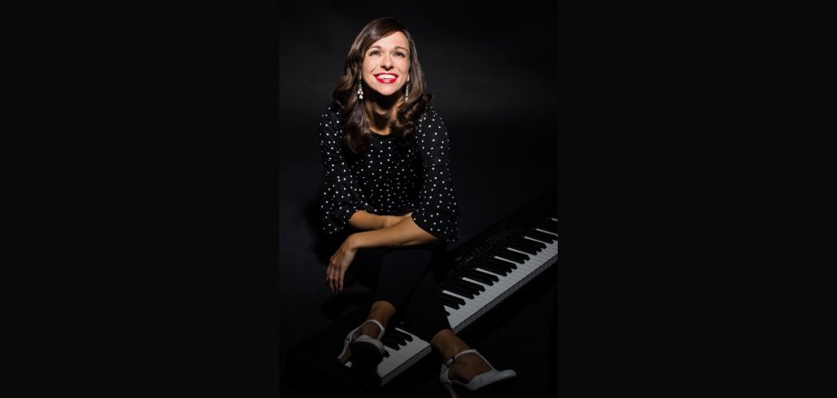 Anna Piechotta sitzt lachend auf einem Klavier.