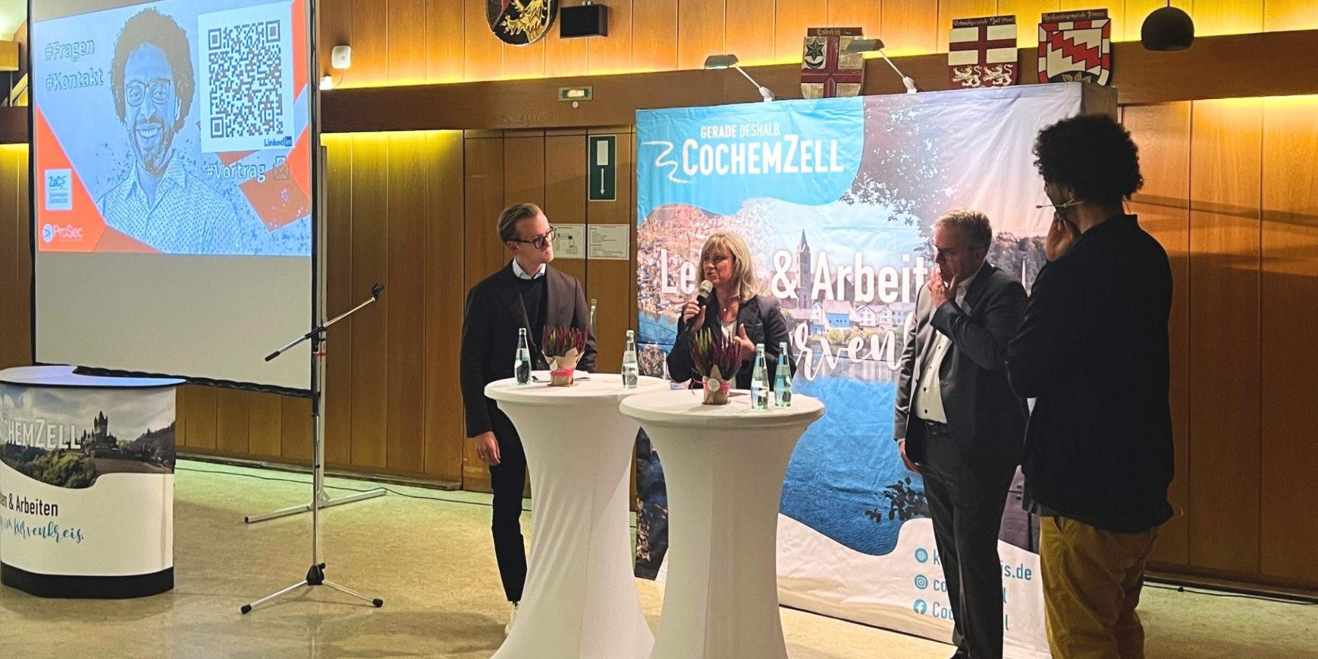 Titel Blogbeitrag Landrätin Beistein, Nico Schnorpfeil, Rainer Thelen und Immanuel Bär stehen nebeneinander während der Podiumsdiskussion.
