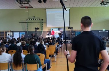 Zwei Schüler laufen durch die Halle, um mit einem Stabmikrofon die Fragen der Schülerinnen und Schüler hörba zu machen.