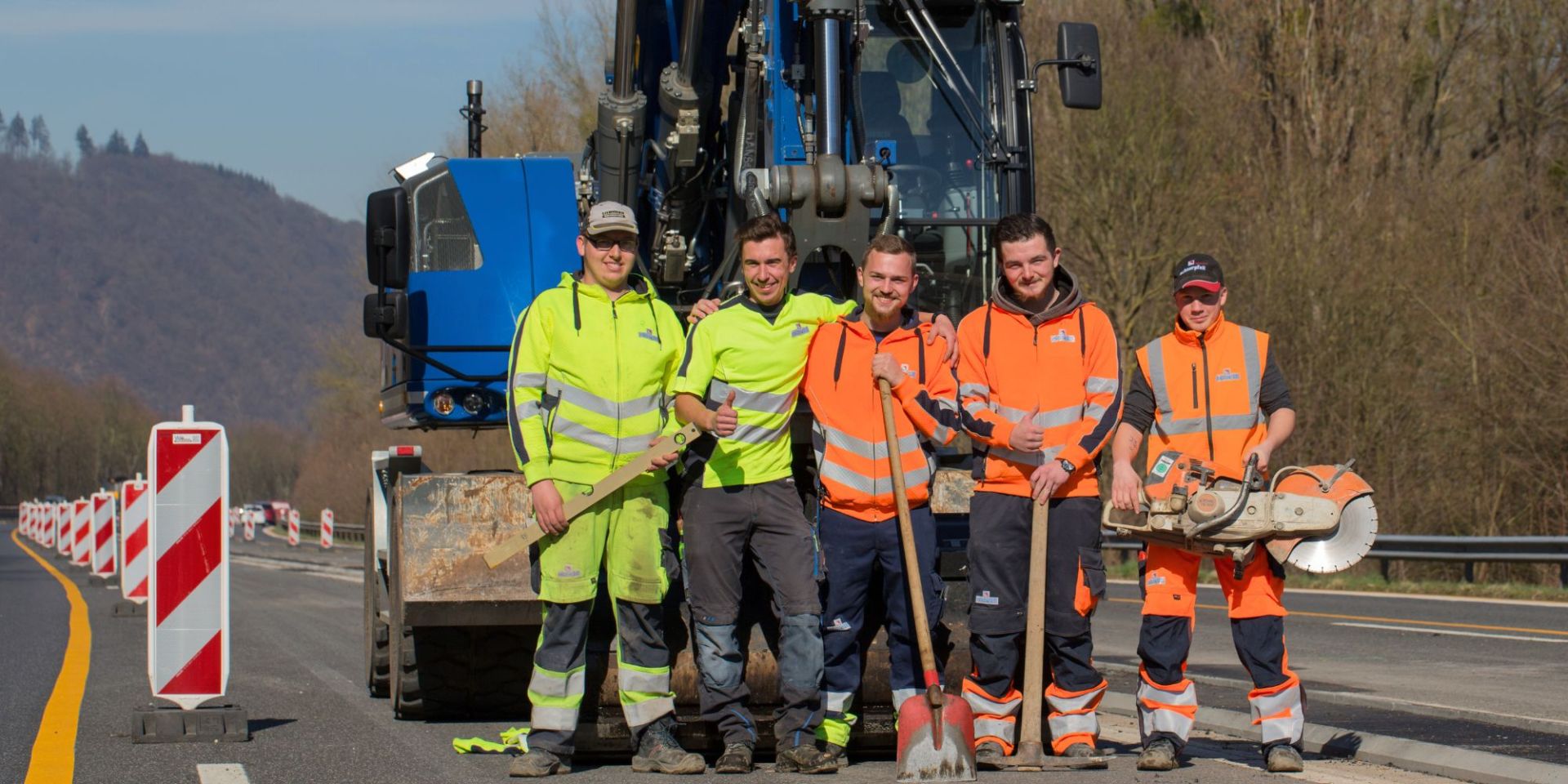 Gruppenbild Straßenbau Azubis Fünf Azubis stehen mit Werkzeugen in der Hand vor einem Bagger von Schnorpfeil.