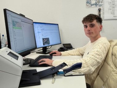 Finn Gerhartz hat die Ausbildung zum Industriekaufmann bei Schnorpfeil erfolgreich abgeschlossen. Im Bild sitzt er am Schreibtisch und schaut in die Kamera.