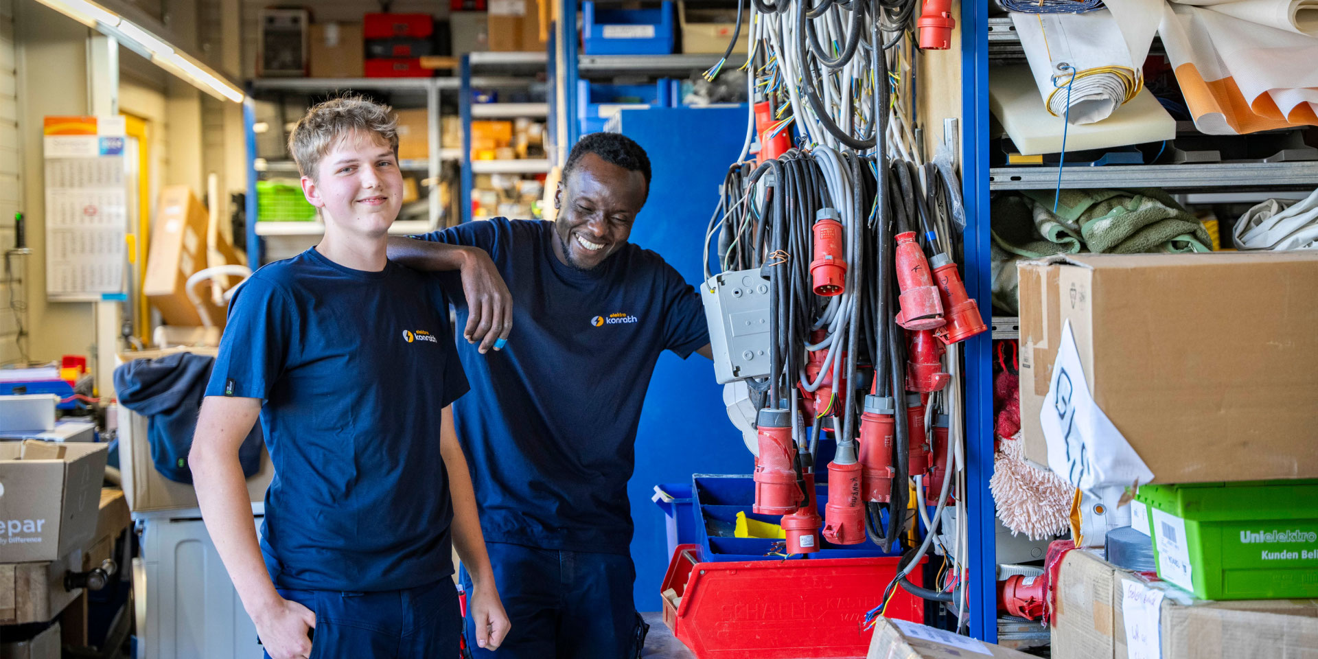 Zwei Mitarbeiter der Firma Elektro Konrath stehen im Lager und lachen.