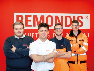 Junge Mitarbeiter bei REMONDIS Mittelrhein vor einer Wand mit Firmenlogo